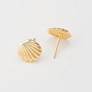 May include: A pair of gold-colored seashell stud earrings. Each earring features a detailed, ridged shell design. The earrings are displayed on a white background, showcasing their bright, reflective surface. The earrings are a classic jewelry item.