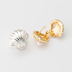 May include: Two seashell-shaped earrings. One is silver with a pearl, the other is gold with a pearl. The gold earring is open, revealing the clasp. The earrings are designed to resemble a clam shell. The earrings are likely made of metal.