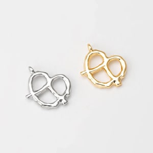 Puede incluir: Dos abalorios de pretzel, uno dorado y otro plateado. Los abalorios tienen forma de pretzel y una superficie texturizada.