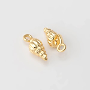 May include: Two gold-colored seashell charms with a loop for attaching to jewelry. The charms are detailed with ridges and curves, resembling miniature conch shells. The background is plain white.