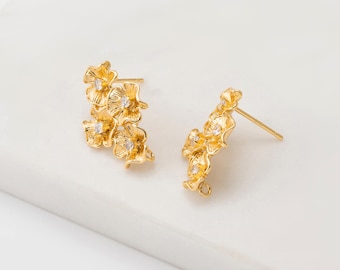 May include: A pair of gold-colored floral earrings. Each earring features a cluster of small, detailed flowers with clear, sparkling accents. The earrings have a post-back design for pierced ears.