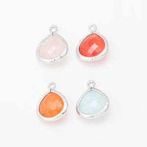May include: Four teardrop-shaped pendants with faceted gemstone centers in pink, red, orange, and light blue. Each gem is set in a silver-colored bezel with a small loop at the top for attaching to a chain or other jewelry component.