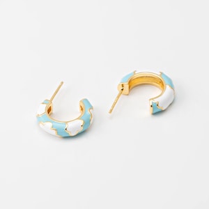 May include: A pair of gold hoop earrings with a blue and white enamel design. The design features white clouds on a light blue background.