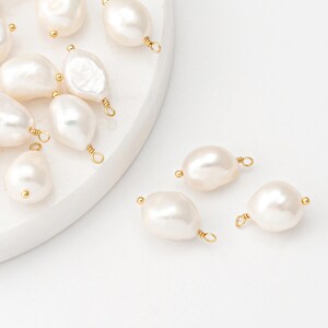 May include: A collection of white baroque pearl beads with gold jump rings. The pearls are oval shaped and have a smooth, glossy finish.