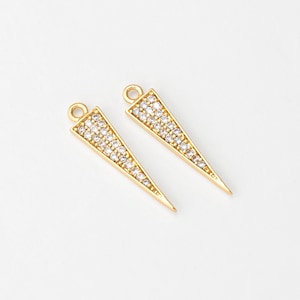 Puede incluir: Dos colgantes triangulares dorados con un lazo en la parte superior. Los colgantes están incrustados con pequeños cristales transparentes, creando un efecto brillante. Ideal para la creación de joyas.