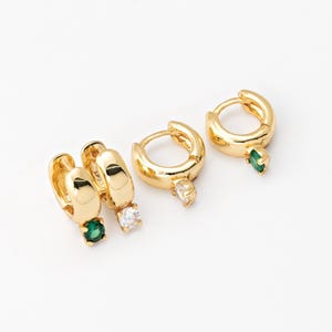 Puede incluir: Tres pares de pendientes de aro de oro con pequeñas piedras preciosas verdes y blancas. Los pendientes son de diferentes tamaños.