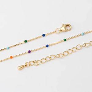 Puede incluir: Un collar de cadena dorada con un acento de cuentas de colores. El collar tiene un cierre de langosta y una cadena extensora.