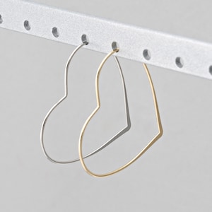 May include: Two heart-shaped hoop earrings. One is silver, the other gold. They hang from a silver bar with evenly spaced holes. The earrings are simple and elegant, suitable for everyday wear.