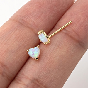 Könnte beinhalten: Ein Paar goldene herzförmige Ohrringe mit weißen Opal-Steinen.