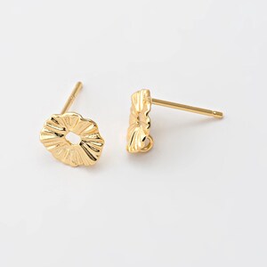 Puede incluir: Un par de postes de pendientes de color dorado con un diseño texturizado y festoneado. Los postes son de metal y tienen un aspecto simple y elegante.