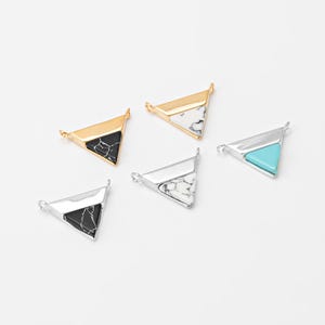 May include: Five triangle-shaped jewelry pendants in gold and silver tones. Each pendant features a different stone inlay: black, white, and turquoise. The pendants have small loops for attaching to a chain or other jewelry component.