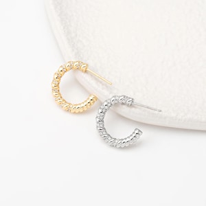 May include: A pair of small hoop earrings with a twisted design. One earring is gold and the other is silver.