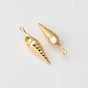 Puede incluir: Dos abalorios de concha de mar de color dorado con un diseño texturizado detallado. Los abalorios tienen un bucle en la parte superior para sujetarlos a joyas u otras manualidades.