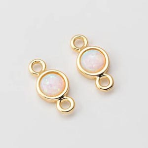 Puede incluir: Dos abalorios conectores de tono dorado con una piedra de ópalo blanca en el centro. Cada abalorio tiene dos bucles para sujetar a las joyas.