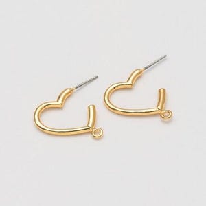 May include: A pair of gold-coloured heart-shaped earrings. Each earring features a post for piercing and a small loop at the base. The earrings are displayed on a white backdrop.