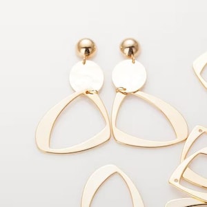 May include: Gold-toned earrings with a geometric design. Each earring features a small ball stud, a circular disc, and a large open triangle shape. Additional gold-colored triangle shapes are scattered around.