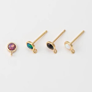 May include: Four gold-toned earring posts with different colored oval-shaped stones. The stones are pink, green, black, and white.