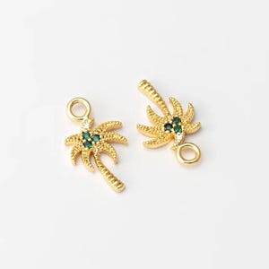 May include: Two gold-colored palm tree charms with green gemstone accents. The charms have a textured surface and a small loop for attaching to jewelry. The palm tree leaves are detailed, and the overall design is tropical.