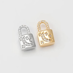 May include: Two lock charms with a crescent moon and stars design. One charm is silver and the other is gold.