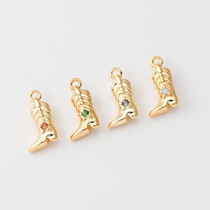 May include: Four gold-colored cowboy boot charms with colorful gemstones. Each charm has a different gemstone color: red, green, gray, and light blue. The charms are arranged diagonally on a white background.