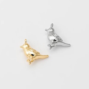 Może przedstawiać: Dwa wisiorki w kształcie ptaków. Jeden jest złoty, drugi srebrny. Oba mają pętlę u góry do zawieszenia. Ptaki są szczegółowe ze skrzydłami, dziobami i stopami. Są umieszczone na białym tle.