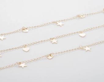 May include: Delicate gold-colored chain necklaces with heart and star charms. The necklaces are displayed on a white surface. The charms are evenly spaced along the chains, creating a simple yet elegant design.
