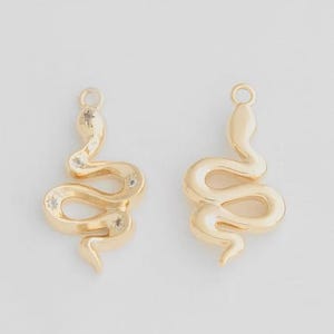 Op de afbeelding: Twee gouden slangenbedels met heldere strasssteentjes. De slangenbedels zijn opgerold en hebben een lus aan de bovenkant om aan sieraden te bevestigen.