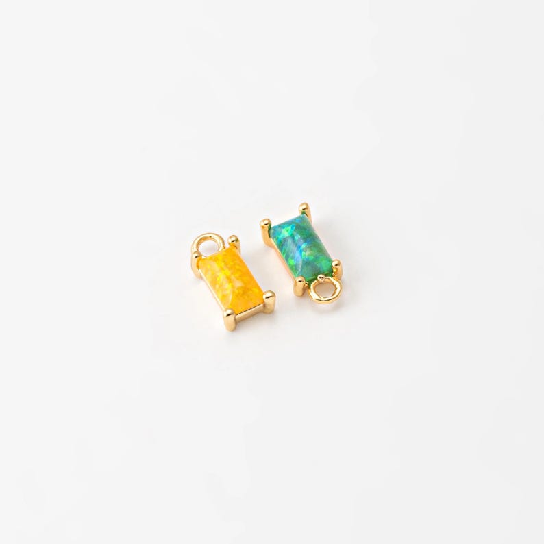 May include: Two gold-toned charms with a rectangular opal stone. One charm is yellow and the other is green.