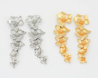 May include: Two pairs of floral drop earrings. One pair is silver-toned, and the other is gold-toned. Each earring features a cascading design of multiple flower shapes, creating a long, elegant silhouette. The earrings are set against a white background.