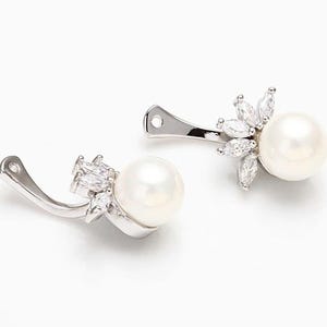 May include: A pair of silver clip-on earrings with a pearl and a cluster of clear cubic zirconia stones.