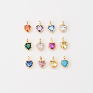 May include: Assortment of 12 gold heart-shaped charms with different colored gemstones. The charms are arranged in two rows of six. The gemstones are red, purple, blue, clear, green, pink, yellow, and turquoise.