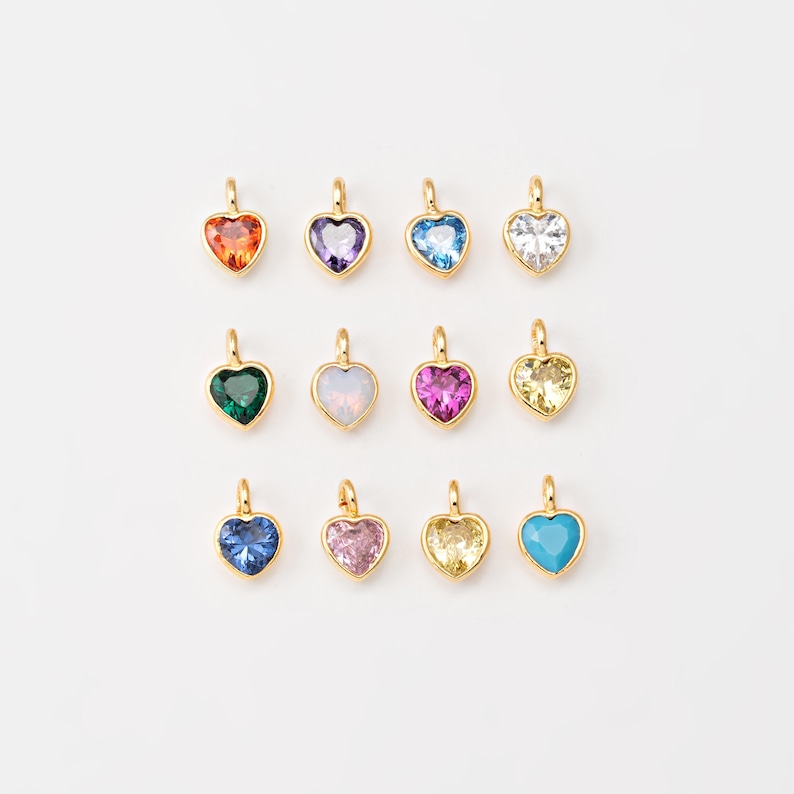 May include: Assortment of 12 gold heart-shaped charms with different colored gemstones. The charms are arranged in two rows of six. The gemstones are red, purple, blue, clear, green, pink, yellow, and turquoise.