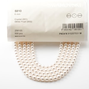 Puede incluir: Un paquete de perlas blancas Swarovski, de 6 mm, con el código de producto 5810. El paquete contiene 500 perlas de cristal blanco. El texto "MADE IN AUSTRIA" está impreso en el paquete.