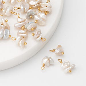 Op de afbeelding: Een verzameling witte barokparels in clusters met goudkleurige draadlussen. De parels zijn onregelmatig van vorm en grootte, en sommige hebben een lichte iriserende glans.