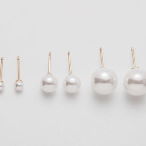 Op de afbeelding: Set van vijf paar parel oorbel studs met gouden pinnen. De oorbellen zijn gerangschikt op grootte, met het kleinste paar links en het grootste paar rechts.