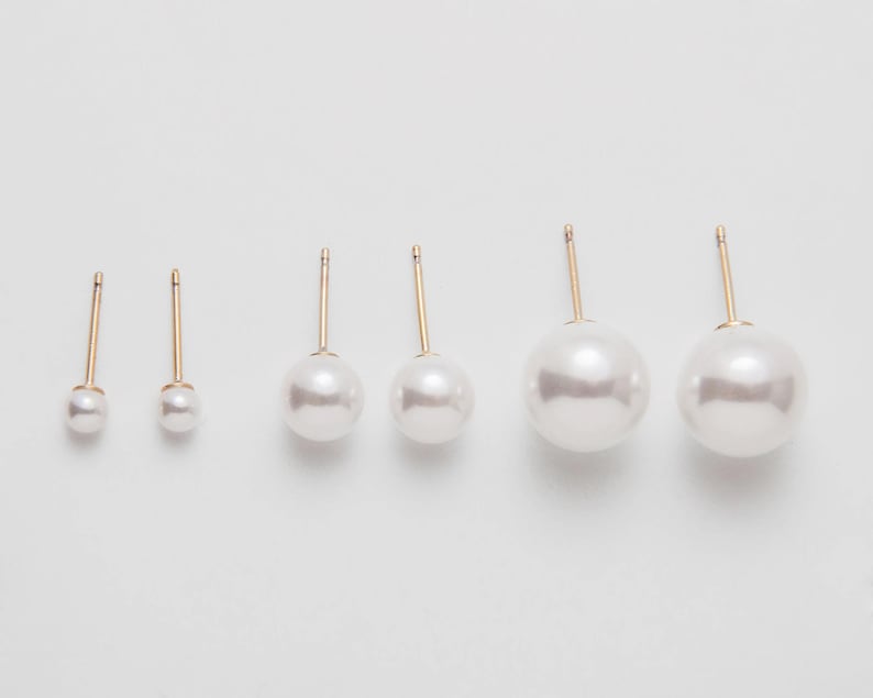 Op de afbeelding: Set van vijf paar parel oorbel studs met gouden pinnen. De oorbellen zijn gerangschikt op grootte, met het kleinste paar links en het grootste paar rechts.