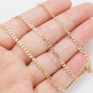 May include: A gold-colored curb chain necklace. The chain is made of small, interlocking links. The necklace is displayed on a light background.