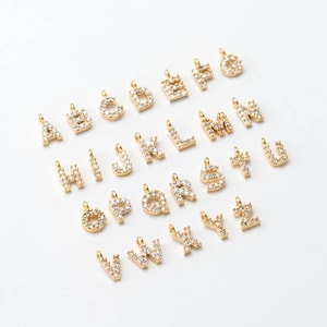 Puede incluir: Un conjunto de 26 abalorios de letras del alfabeto de tono dorado, cada letra está incrustada con brillantes diamantes de imitación transparentes. Los abalorios son perfectos para agregar un toque personalizado a collares, pulseras o llaveros.