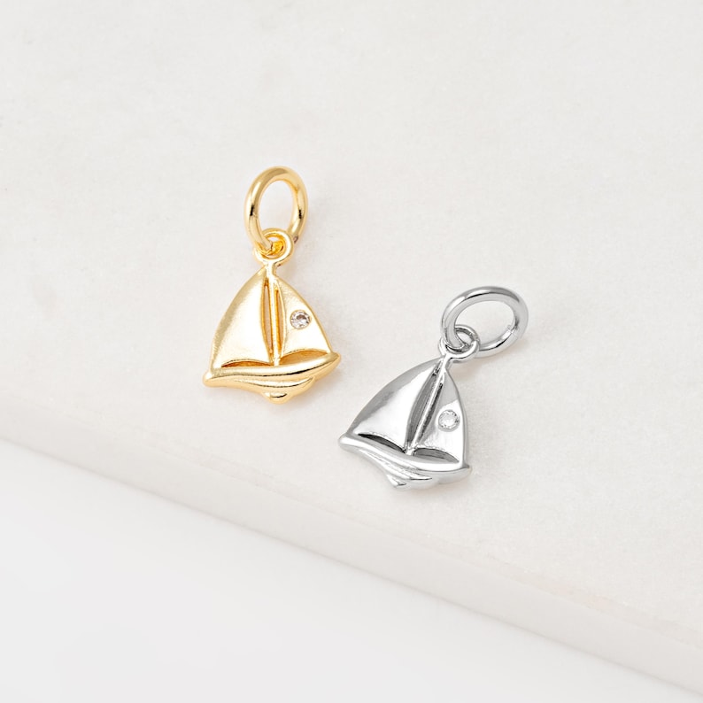 May include: Two sailboat charms, one gold and one silver, with a small clear crystal in the center of each sail.