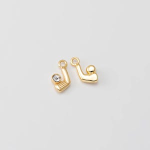 May include: Two gold-colored golf-themed charms. One charm features a golf club with a clear crystal accent, and the other depicts a golf ball. Both charms have a small loop at the top for attaching to jewelry.