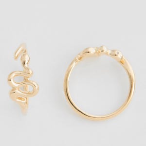 May include: Two gold rings. One is a band with a snake design, and the other is a ring with a snake-shaped ear cuff. The jewellery is set against a white background.