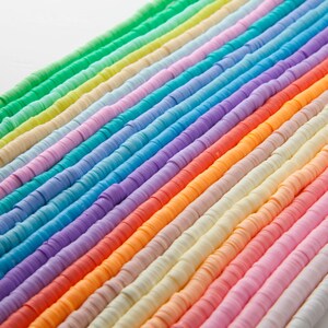 May include: Rows of colorful, flat polymer clay beads in a rainbow of colors. The beads are arranged diagonally across the frame, showcasing a spectrum from green to purple, orange, and pink. These beads are ideal for jewelry making and crafting.
