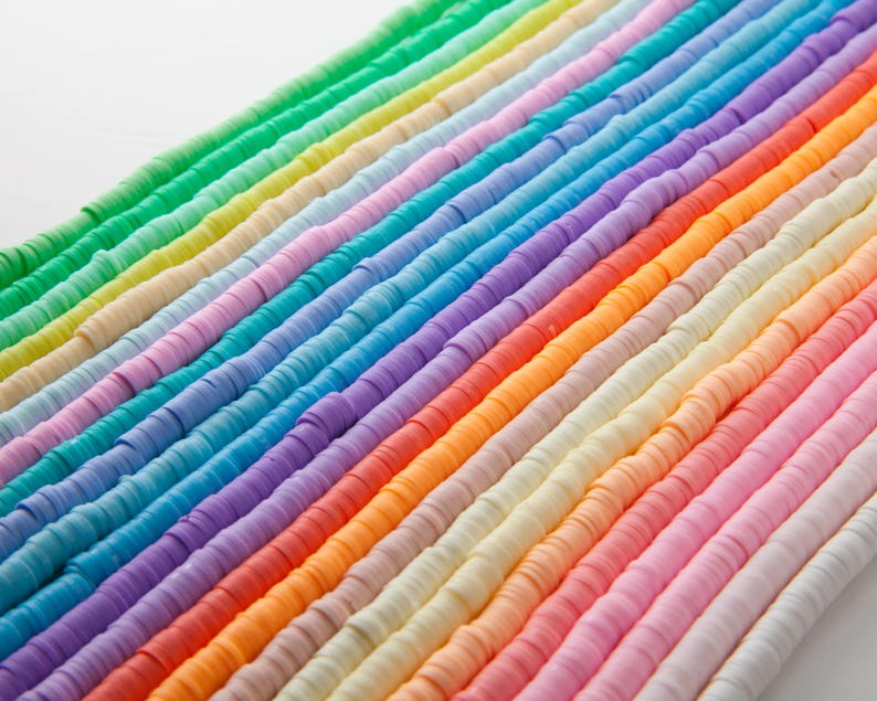 May include: Rows of colorful, flat polymer clay beads in a rainbow of colors. The beads are arranged diagonally across the frame, showcasing a spectrum from green to purple, orange, and pink. These beads are ideal for jewelry making and crafting.