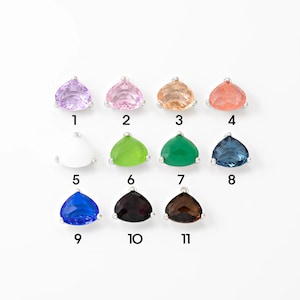 Puede incluir: Una colección de once colgantes de piedras preciosas en varios colores, incluyendo lavanda, rosa, melocotón, coral, blanco, verde, turquesa, azul y marrón. Cada piedra triangular está engastada en un engaste de metal plateado y numerada del 1 al 11.