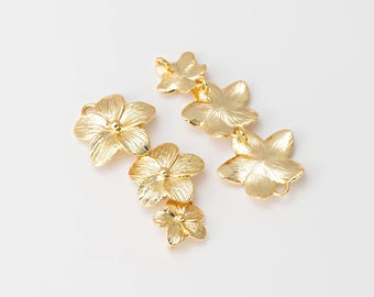 May include: Gold-colored floral charms with detailed petal textures. The charms are in the shape of flowers, with multiple charms connected together. The charms are on a white background.
