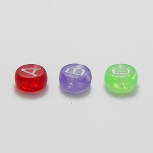 Könnte beinhalten: Drei durchscheinende, runde Perlen in Rot, Lila und Grün. Jede Perle hat einen weißen Buchstaben: A, B und C. Die Perlen sind gleichmäßig auf einem weißen Hintergrund verteilt. Diese Perlen eignen sich für die Schmuckherstellung oder Bastelarbeiten.