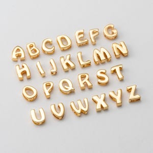 Op de afbeelding: Gouden alphabet letter charms, elke letter is individueel gemaakt en heeft een licht verhoogd ontwerp. De letters zijn in alfabetische volgorde gerangschikt.