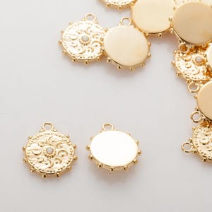 May include: Gold-colored metal charms with a round shape. Some charms have a textured, ornate design with a small, round, white accent in the center. Other charms are smooth and plain. All charms have a small loop at the top for attaching to jewelry.