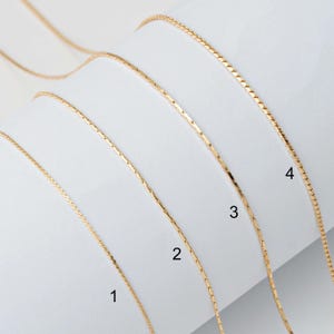 Puede incluir: Cuatro cadenas de oro de diferentes grosores dispuestas sobre una superficie blanca. Las cadenas están numeradas del 1 al 4, siendo la cadena más gruesa la número 1 y la cadena más fina la número 4.