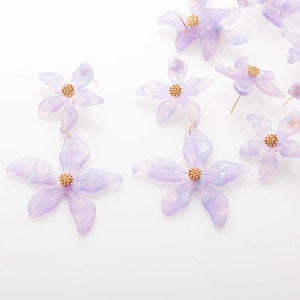 May include: A collection of delicate, light purple flower earrings with gold-colored centers. The earrings are made of a translucent material, and the petals have a subtle, marbled effect. The earrings are designed to resemble flowers.